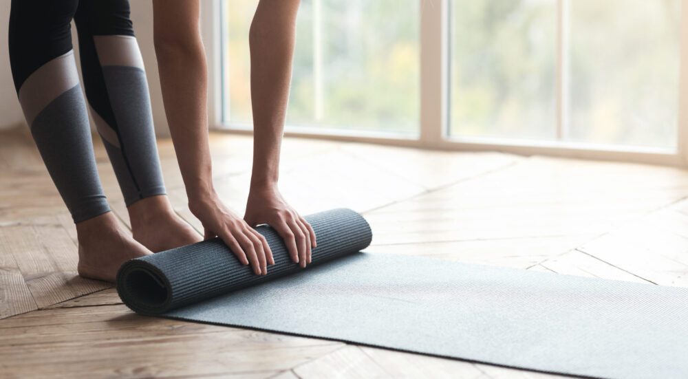 Cropped photo of girl getting ready before morning yoga practice, placing her yoga mat on floor at fitness studio, panorama with copy space