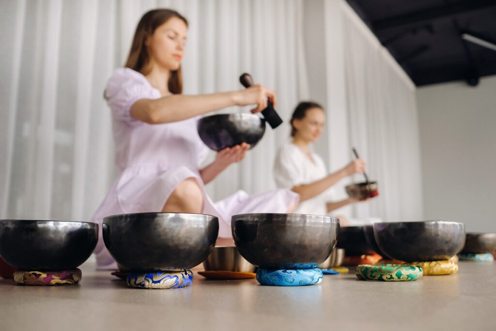 Two female yoga teachers play on Tibetan bowls in the gym during a yoga retreat.