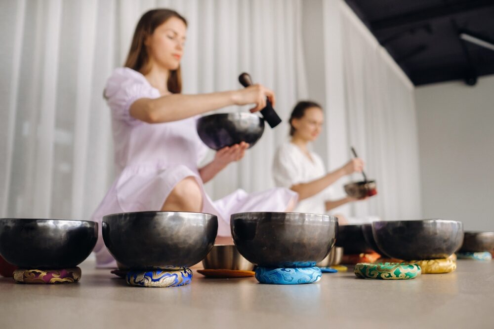 Two female yoga teachers play on Tibetan bowls in the gym during a yoga retreat.