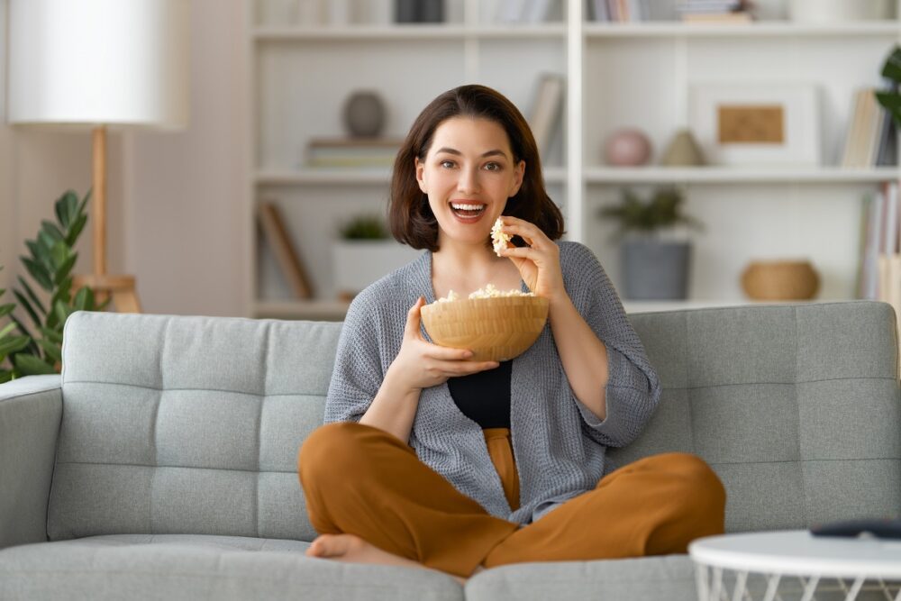 Young woman watching TV, movies with popcorn in the evening. Girl spending time at home.