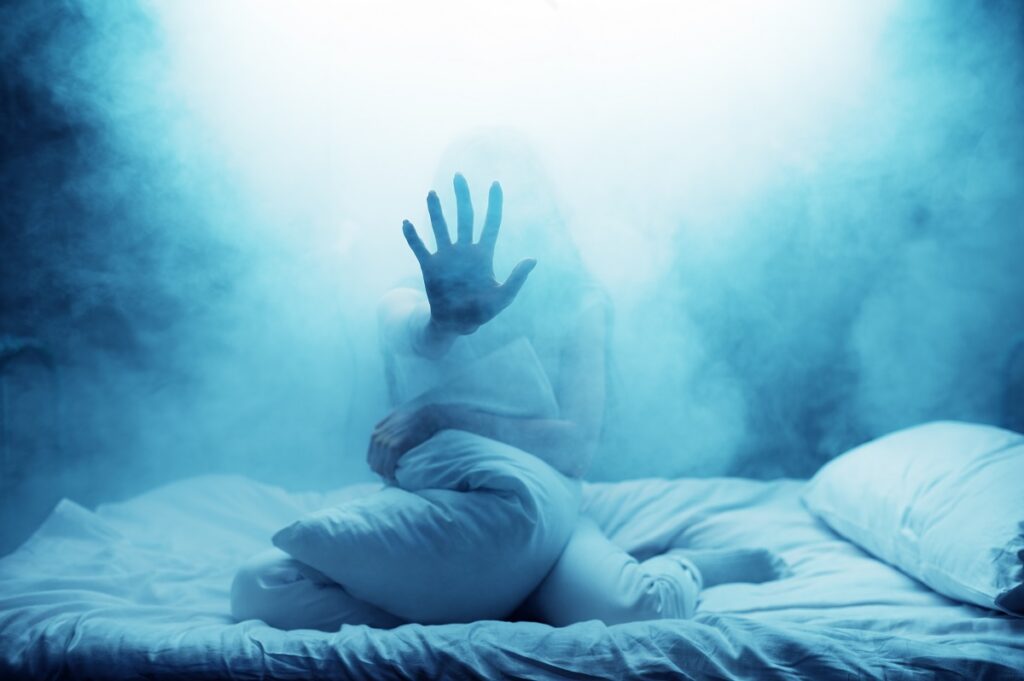 Psycho woman show hand in bed, dark smoky room on background. Psychedelic person having problems every night, depression and stress, sadness, psychiatry hospital