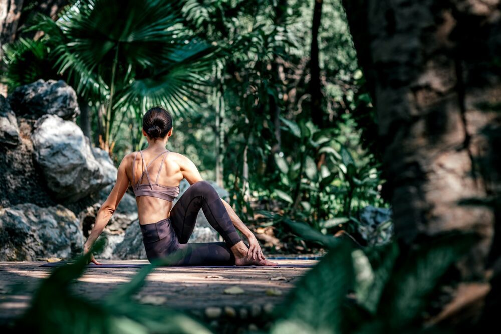 Full-length shot of caucasian woman sitting in Seated Twist pose, Ardha Matsyendrasana while practicing yoga outdoors, in a garden. Healthy lifestyle and relaxation concept