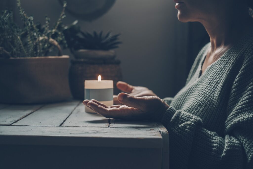 Woman at home in zen meditation activity and candlelight in background. One female people with hands up pray or meditate alone in dark light indoor. Concept of healthy mental lifestyle. Nature