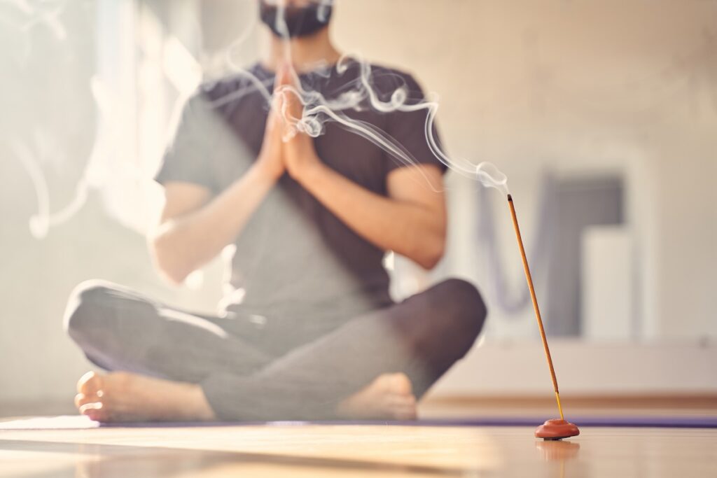 Close up of man sitting in lotus position on the floor with aroma stick