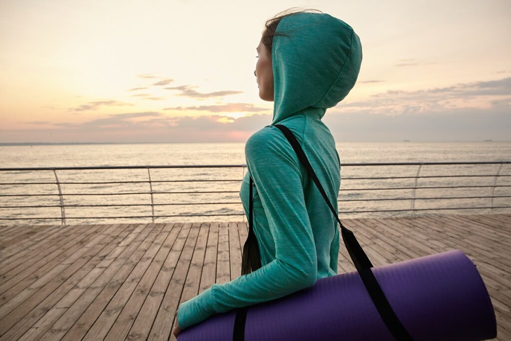 Woman walking at the seaside, going to practicing yoga and makes morning stretching , dressed sportwears. Health care concept.
