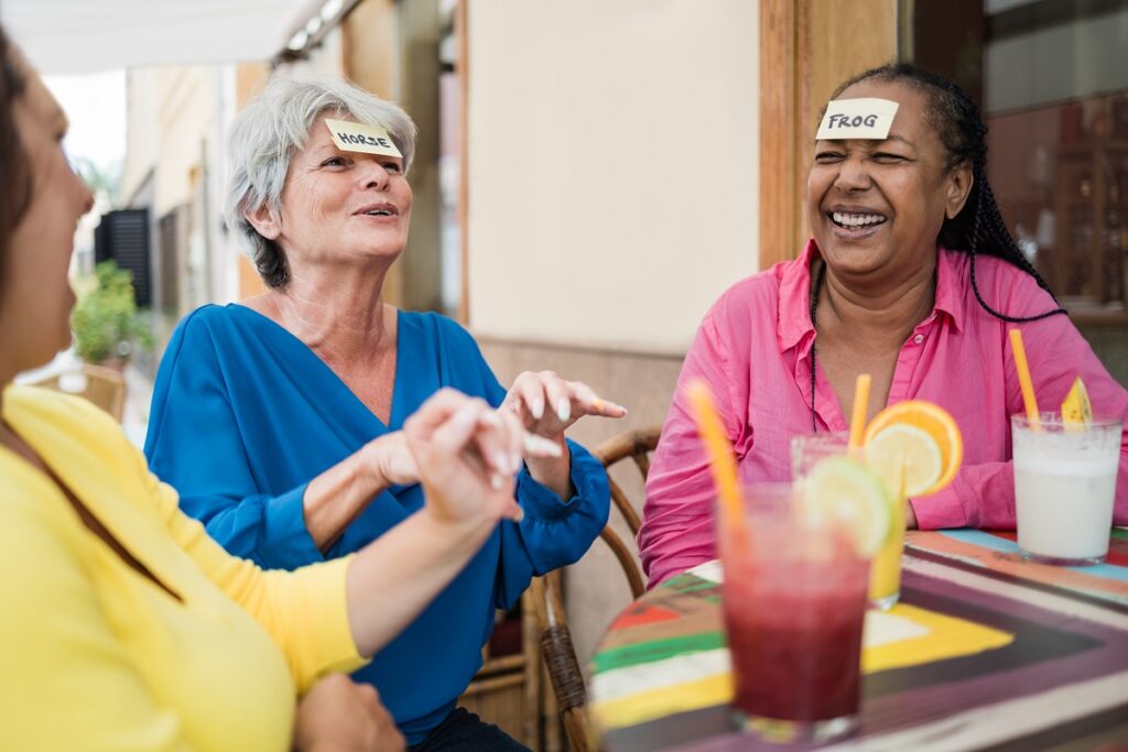 Multiracial senior friends having fun playing together guess who forehead game at bar restaurant - Focus on african woman face