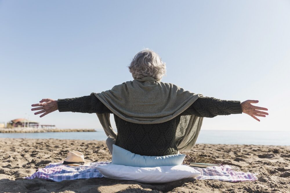 Mindful senior woman staying on the sand, watching the sea